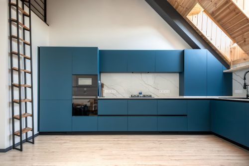 Sleek kitchen design with built-in oven and microwave, angled ceiling, and modern matte blue cabinetry. Ideal solution for attic-style compact living.